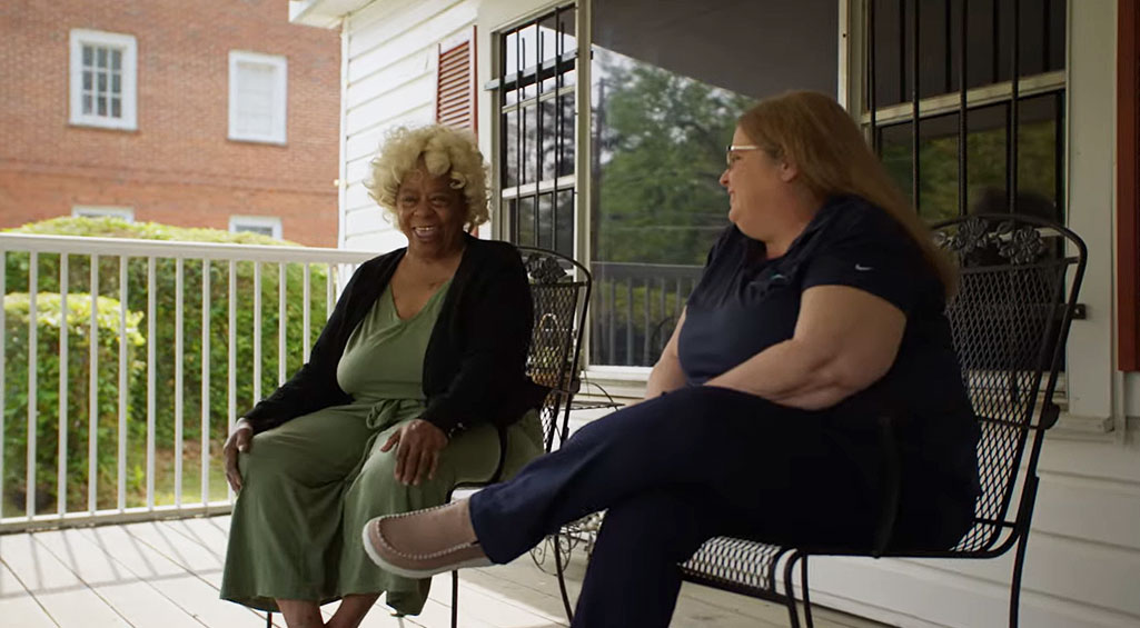 Woman sitting on her front porch, smiling and talking with Monogram Health nurse.