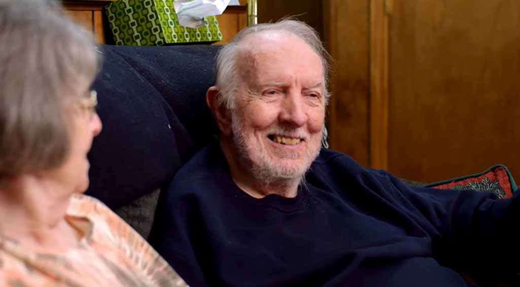 Husband and wife sitting on couch talking about their Monogram Health experience.