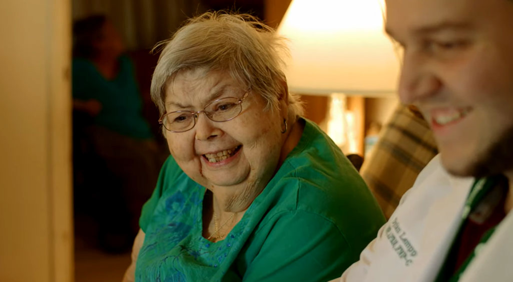 Woman smiling while talking with her doctor on couch in her living room.