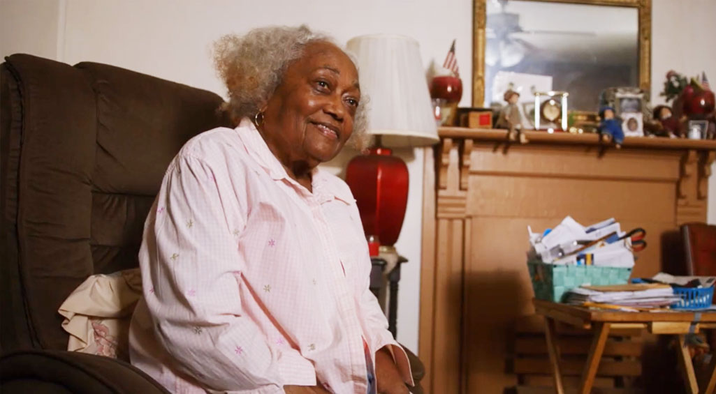 Woman sitting in her living room, smiling.